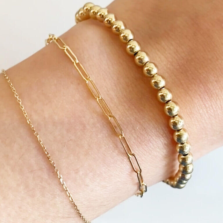 Gold Bead Bracelet and Paperclip Chain Bracelet on a wrist.